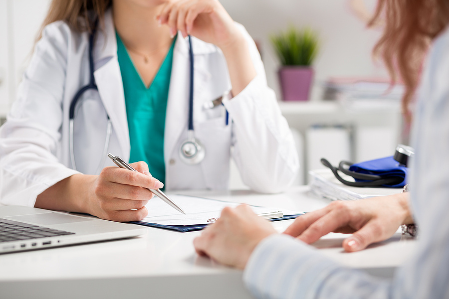 doctor at a desk writing, with a patient on the other side of the desk